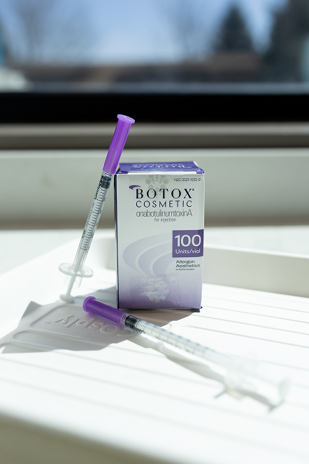A box of Botox Cosmetic with two syringes having purple caps, placed on a white tray. Sunlight casts soft shadows, creating a clinical yet serene tone.